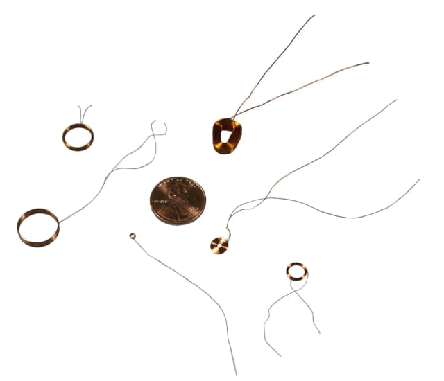 Six various size miniature self-supporting coils next to a penny for size reference